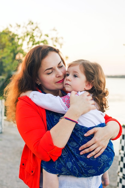 Family portrait of wrapping baby toddler girl in blue sling carrier and mother hugs