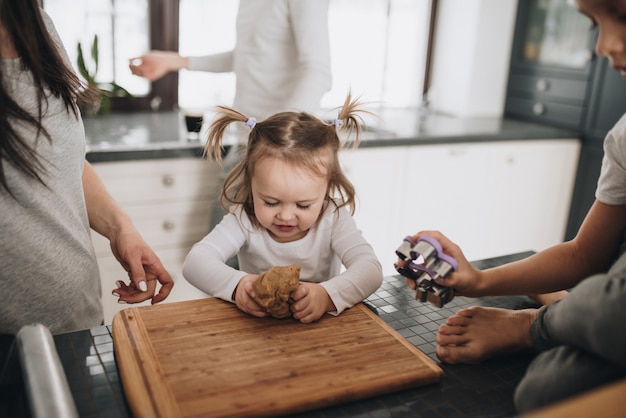 The family prepares gingerbread cookies in the kitchen. Dad, mom, son, daughter, brother and sister. Knead dough, cookie cutters, New Year, Christmas, holiday dinner. Gray homewear.