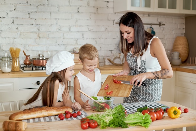 Family prepares lunch in the kitchen. Mom teaches her daughter and son to prepare a Salad of fresh vegetables. Healthy natural food, vitamins for children