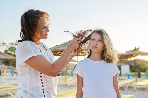 Family relaxing weekend on the beach mature mother combing hair of her preteen daughter caring love care parent and child