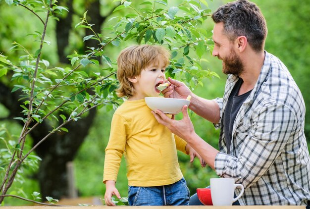 Family rest time son and father eating outdoor happy fathers day Little boy with dad eat cereal Morning breakfast Tasty food healthy food and dieting Dairy products help and support