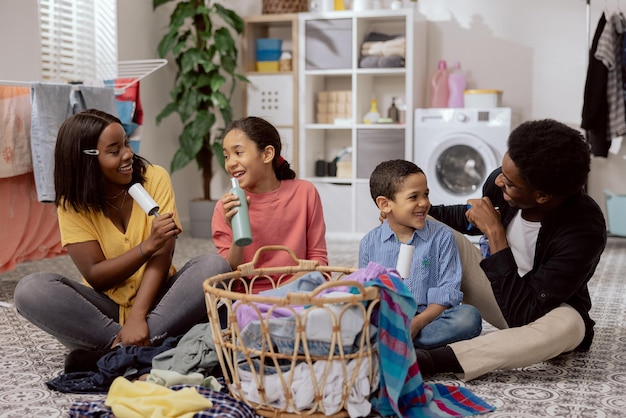 A family sits on the laundry room floor sorting clothes before putting them in the washing machine playing together during household chores singing to random objects