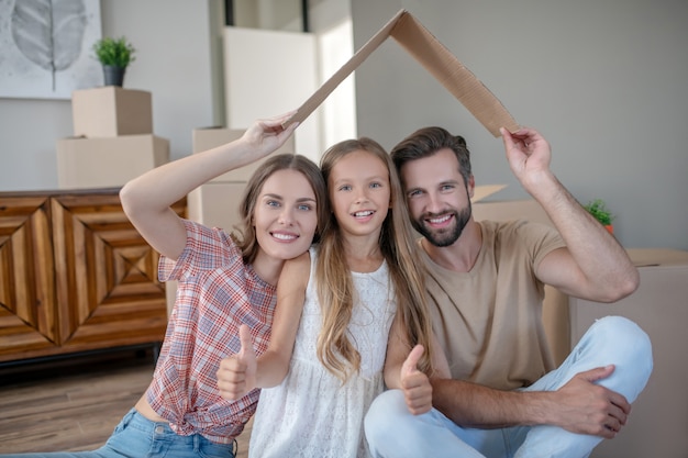 Family sitting under paper roof and smiling