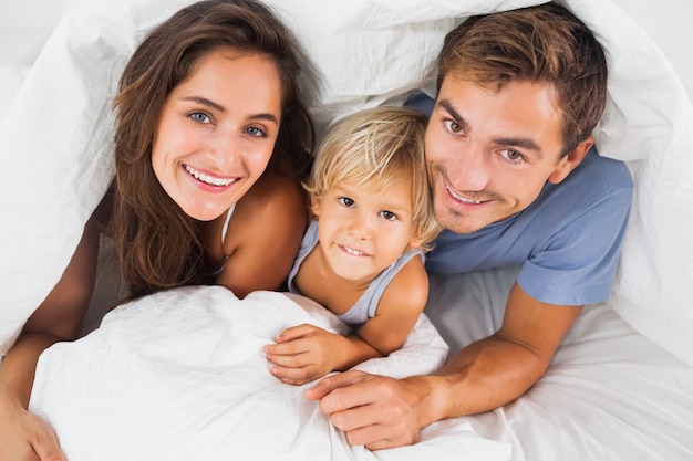 Family smiling under the duvet on the bed