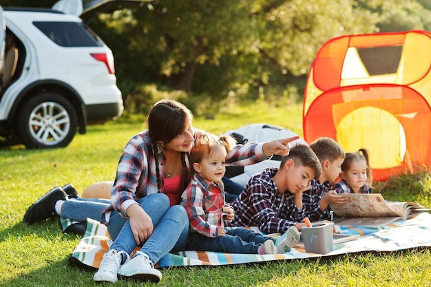 Family spending time together Mother with four kids outdoor in picnic blanket against their american suv