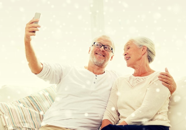 family, technology, age and people concept - happy senior couple with smartphone taking selfie at home