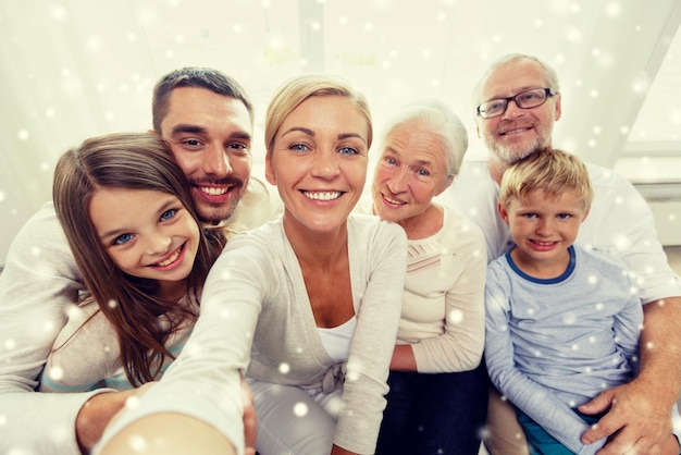 family, technology, generation and people concept - happy family sitting on couch and taking self portrait with camera or smartphone at home