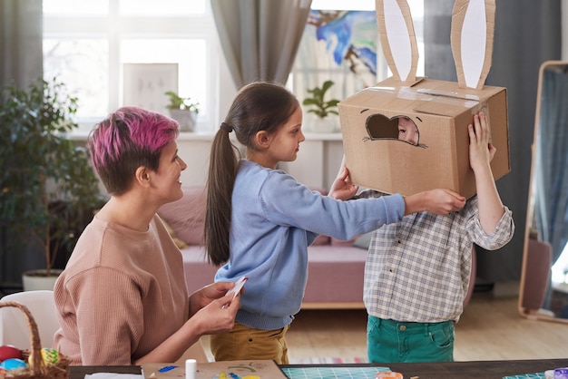 Family of three making rabbit costume from cardboard box they preparing for Easter holiday