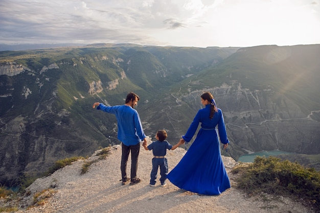 Family of three people stands on the mountain gorge during sunset in Dagestan