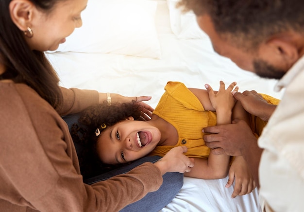 Family tickle playing and girl with happy parents bonding with quality time together at a home Laughing smiling and happiness of a child smile with a mom father and care on a bedroom bed