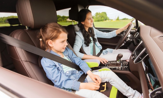 family, transport, road trip and people concept - happy woman with little daughter driving in car