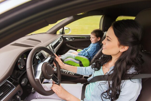 family, transport, road trip and people concept - happy woman with little daughter driving in car