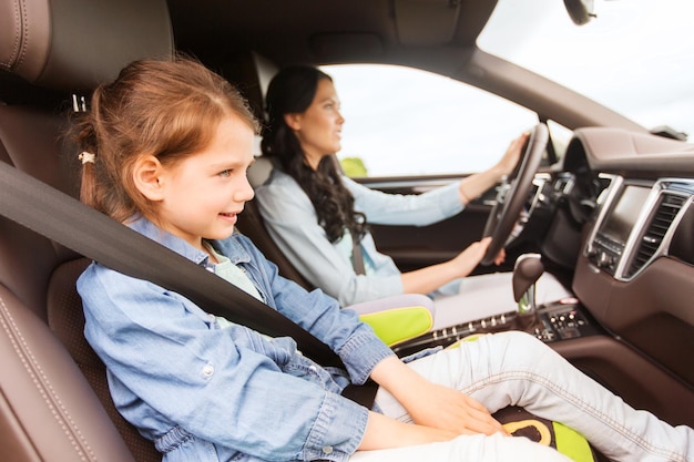 family, transport, road trip and people concept - happy woman with little daughter driving in car