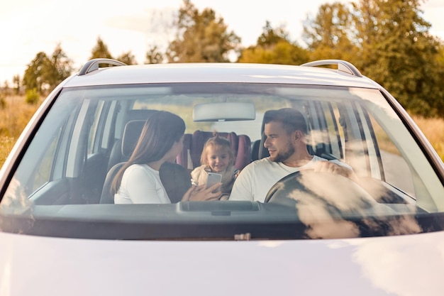 Family transport safety road trip and people portrait of happy man and woman with little child driving in car traveling together mother showing cell phone to child