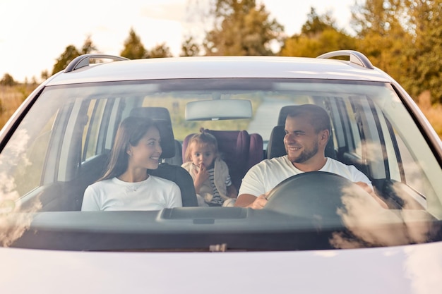 Family transport safety road trip Portrait of happy man and woman with little child in baby seat driving in car expressing positive emotions traveling together smiling