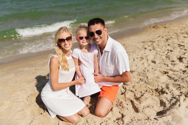 family, vacation, adoption and people concept - happy man, woman and little girl in sunglasses on summer beach