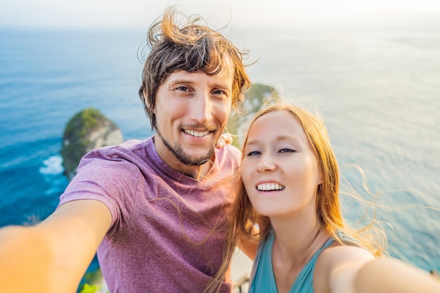 Family vacation lifestyle Happy couple man and woman stand at viewpoint Look at beautiful beach under high cliff Travel destination in Bali Popular place to visit on Nusa Penida island