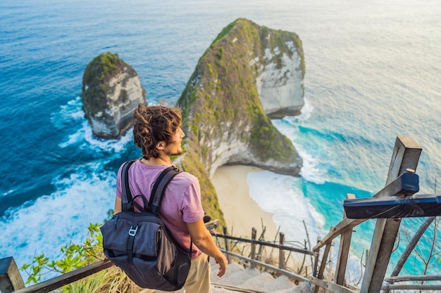 Family vacation lifestyle Happy man stand at viewpoint Look at beautiful beach under high cliff Travel destination in Bali Popular place to visit on Nusa Penida island