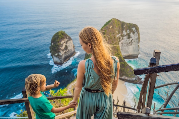 Family vacation lifestyle Happy mother and son stand at viewpoint Look at beautiful beach under high cliff Travel destination in Bali Popular place to visit on Nusa Penida island