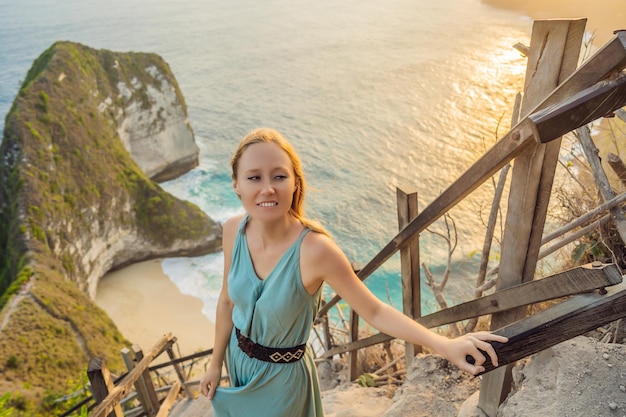 Family vacation lifestyle Happy woman stand at viewpoint Look at beautiful beach under high cliff Travel destination in Bali Popular place to visit on Nusa Penida island