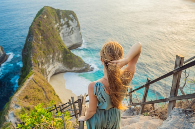 Family vacation lifestyle Happy woman stand at viewpoint Look at beautiful beach under high cliff Travel destination in Bali Popular place to visit on Nusa Penida island