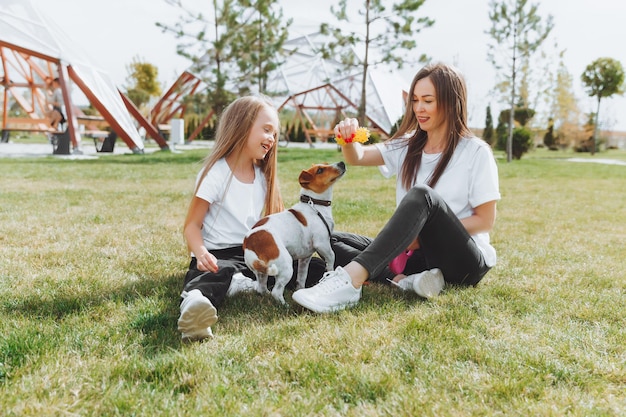 Family walk in the autumn park Outdoor entertainment Mother and daughter walk the dog on a sunny warm autumn day a child plays with a jack Russell terrier in the park