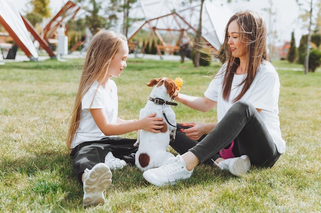 Family walk in the autumn park Outdoor entertainment Mother and daughter walk the dog on a sunny warm autumn day a child plays with a jack Russell terrier in the park