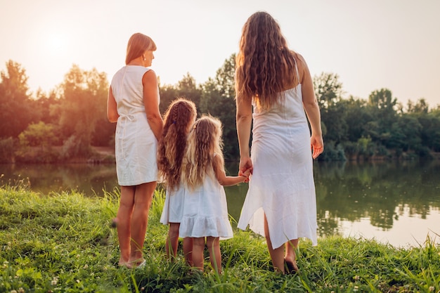 Family walking by summer river at sunset