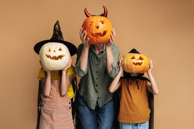 Family wearing costumes posing and having fun holding carved pumpkin isolated on beige background