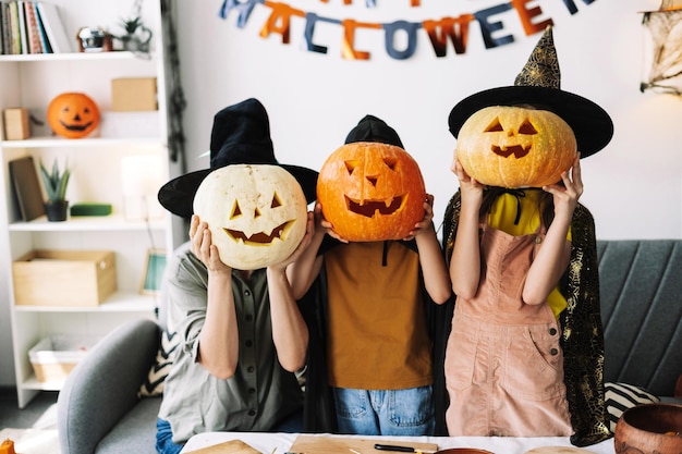 Family wearing halloween costumes holding carved pumpkins over faces