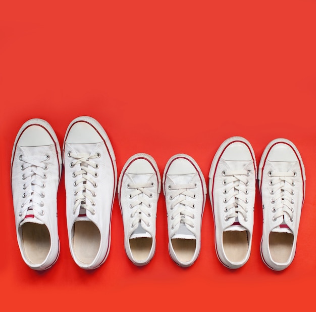 Family of white shoes. Mom's, daddies, children's sneakers stand red background