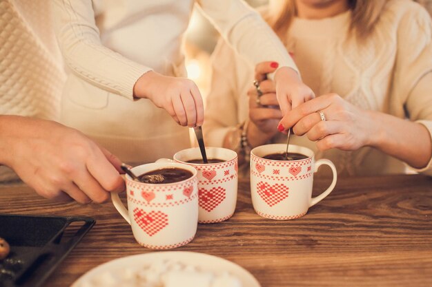 Family in white sweaters cook and drink cocoa with marshmallows Closeup hands and cups