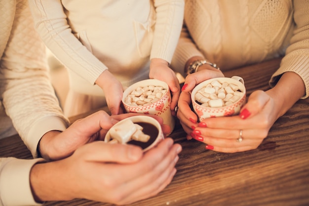 Family in white sweaters cook and drink cocoa with marshmallows