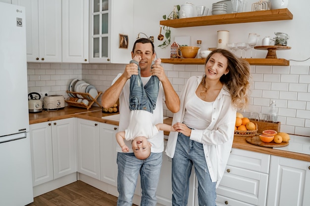 a family with a baby in jeans and white Tshirts are playing in the kitchen