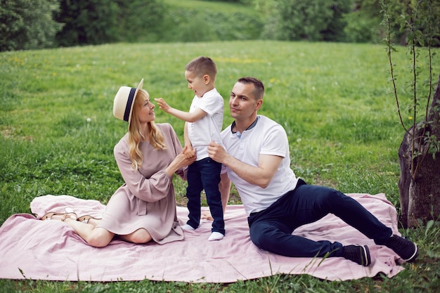 Family with a child a boy of 4 years old sitting on a green field under a tree in summer on a blanket