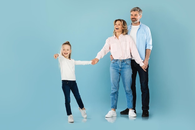 Family with daughter holding hands pointing finger over blue background