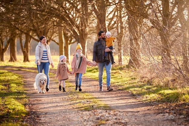 Family With Down Syndrome Daughter Walking With Pet Dog In Autumn Or Winter Countryside Together