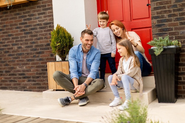 Family with a mother father son and daughter sitting outside on the steps of a front porch of a brick house