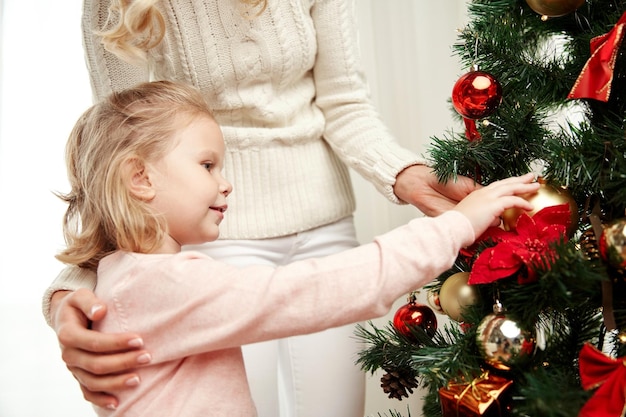 family, x-mas, winter holidays and people concept - happy mother and little daughter decorating christmas tree at home