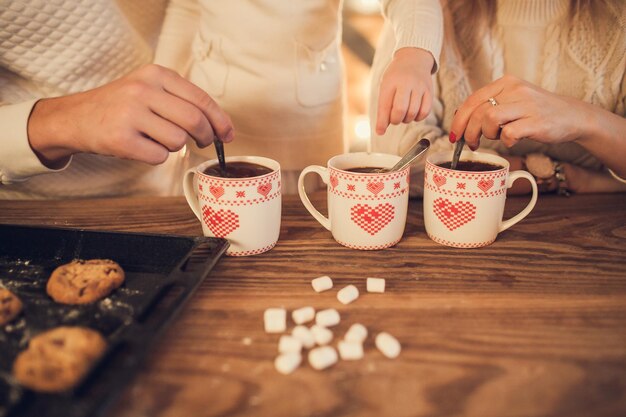 Familywhite sweaters cook and drink cocoa with marshmallows Closeup hands and cups