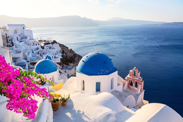 Famous Santorini iconic view Blue domes and traditional white houses with bougainvillea flowers Oia village Santorini island Greece