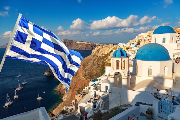 Famous Santorini view Three blue domes and traditional white houses with Greek flag Oia village Santorini island Greece