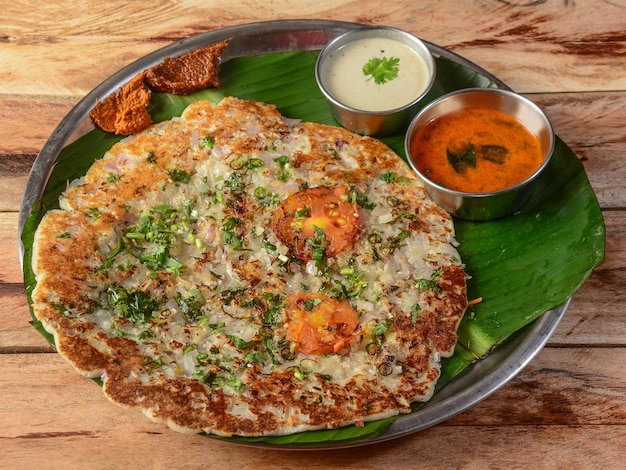 Famous South Indian Food Onion Uttapam or ooththappam is a dosa like dish made by dosa batter served with coconut chutney and sambar selective focus