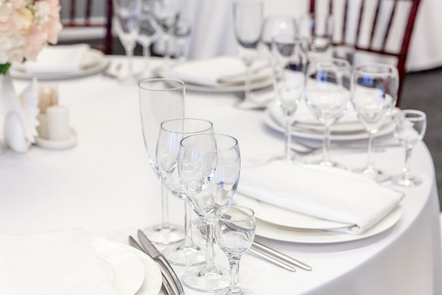 Fancy table set for dinner with napkin glasses in restaurant, luxury interior background. Wedding elegant banquet decoration and items for food arranged by catering service on white tablecloth table.