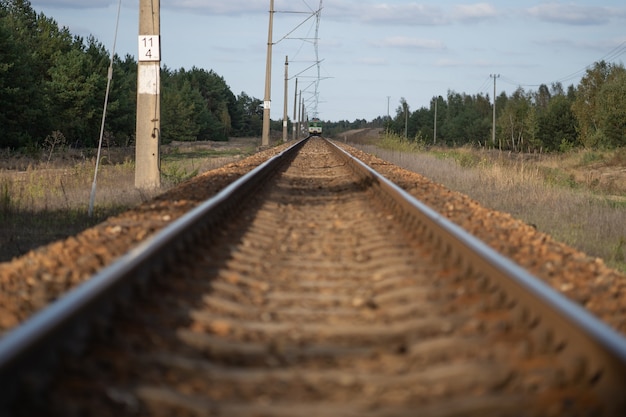 Far away on the horizon, the locomotive of the train is moving towards the camera along the railway rails on a clear summer day