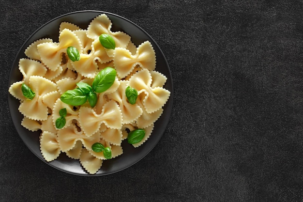 Farfalle cooked pasta with basil green leaves on dark plate on dark background top view space to copy textxA