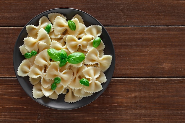 Farfalle cooked pasta with basil green leaves on wooden brown plank tabletop background top view space to copy text