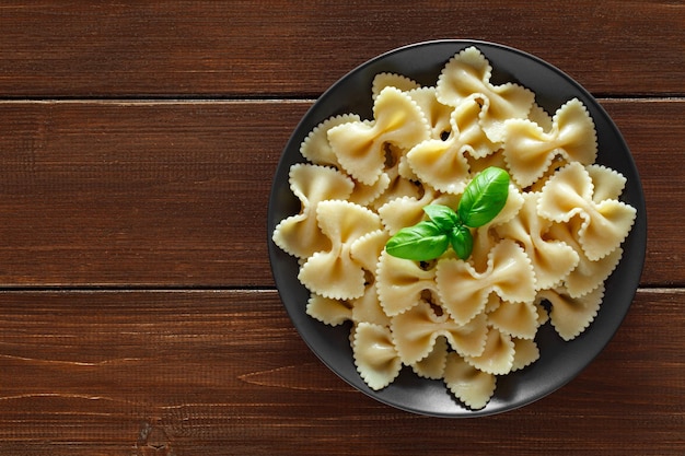 Farfalle cooked pasta with basil green leaves on wooden brown plank tabletop background top view space to copy textxA