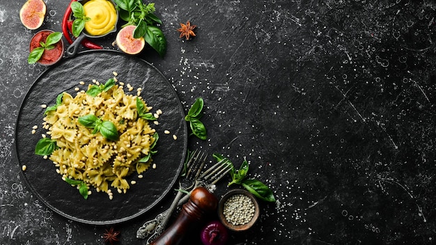 Farfalle pasta with pesto sauce and basil in a black stone plate Top view Free space for your text