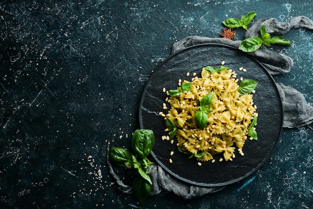 Farfalle pasta with pesto sauce and basil in a black stone plate Top view Free space for your text